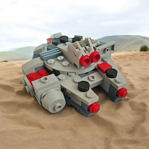 May include: A miniature model of a spaceship constructed from gray, red, and black building blocks. The model features circular and rectangular components, with red exhaust ports and black circular details. The spaceship is set on a sandy surface.