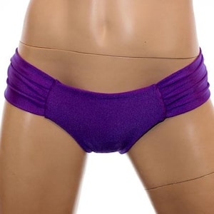 May include: A pair of purple bikini bottoms. The bottoms are a solid, vibrant purple color with a ruched detail on the sides. The fabric appears to have a slight sheen.