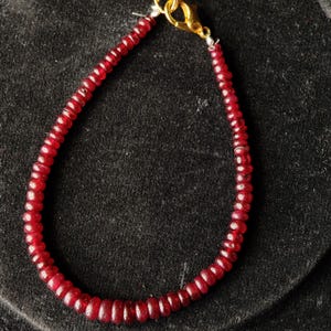 Peut inclure: Un bracelet composé de petites pierres précieuses rondes et rouge foncé. Les perles sont enfilées sur un fin fil argenté et fixées par un fermoir doré. Les perles uniformes créent un aspect lisse et élégant. C'est un bijou.