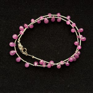 May include: A delicate necklace featuring a thin silver chain adorned with numerous small, teardrop-shaped pink gemstones spaced evenly along the length. The piece includes a silver lobster claw clasp for secure fastening and closure.