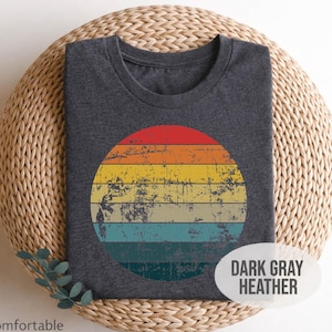 Peut inclure: T-shirt gris foncé chiné avec un motif de cercle multicolore vieilli. Le cercle présente des rayures horizontales rouges, orange, jaunes, vertes et bleues. Le t-shirt est présenté sur un tapis circulaire tissé. Le texte "Soft & Comfortable" est visible.