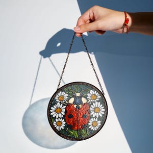 Ladybug glass suncatcher with daisy flowers glowing in sunlight, decorative spring and summer window ornament