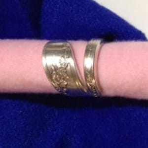 May include: A silver spoon ring with a floral design. The ring is made from a bent spoon and is a unique piece of jewelry.