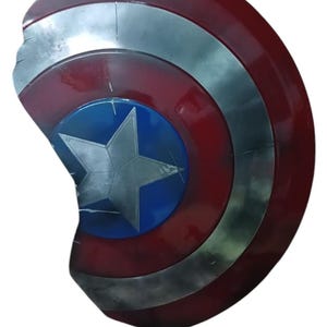 May include: A red, white, and blue shield with a silver star in the center. The shield has a circular design with concentric rings of red, silver, and blue. The shield appears to be made of metal and has a weathered appearance.