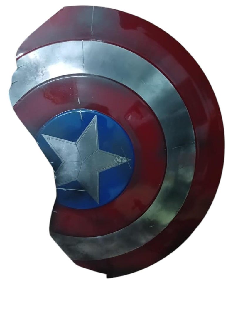 May include: A red, white, and blue shield with a silver star in the center. The shield has a circular design with concentric rings of red, silver, and blue. The shield appears to be made of metal and has a weathered appearance.