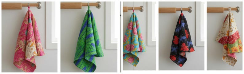 K&ouml;nnte beinhalten: Eine Sammlung von f&uuml;nf dekorativen K&uuml;chent&uuml;chern, die an einer Holzstange h&auml;ngen. Die T&uuml;cher weisen verschiedene farbenfrohe Blumen- und geometrische Muster in Rosa, Gr&uuml;n, Blau, Schwarz und Rot auf. Jedes Tuch ist etwa 50 cm lang.