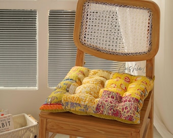 Peut inclure: Chaise en bois avec dossier en cannage et coussin à motifs. Le coussin présente des tissus jaunes, rouges et oranges. La chaise est près d'une fenêtre avec des stores horizontaux. Le mot "Cushie" est visible.