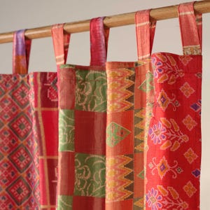 Könnte beinhalten: Bunte Stoffvorhänge mit verschiedenen Mustern, darunter geometrische und florale Designs. Die Vorhänge sind in Rot-, Grün-, Orange- und Lilatönen gehalten und hängen an einer Holzstange. Die Vorhänge sind aus leichtem Material.