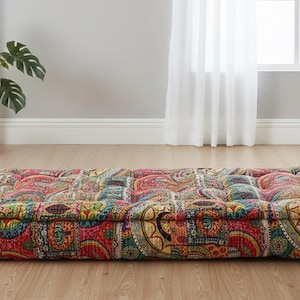 May include: A colourful, rectangular floor cushion with a paisley design in red, yellow, green, and blue. The quilted cushion has a thick, padded appearance, suitable for seating or lounging. The cushion is on a wooden floor.