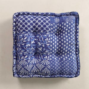 Könnte beinhalten: Quadratisches blaues Bodenkissen mit Patchwork-Design. Das Kissen weist verschiedene Muster auf, darunter Punkte, florale Motive und geometrische Formen, in Blau- und Weißtönen. Die Kanten sind mit einem dunkelblauen Rand versehen.