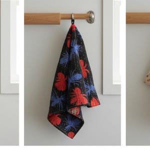 K&ouml;nnte beinhalten: Drei dekorative Handt&uuml;cher h&auml;ngen an einer Holzstange. Die Handt&uuml;cher zeigen florale und abstrakte Muster in verschiedenen Farben, darunter Blau, Rosa, Rot und Schwarz. Jedes Handtuch ist gefaltet und an einem Metallring aufgeh&auml;ngt.