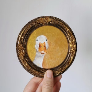 Small round painting of a goose portrait on shimmering gold, permanently attached to a handmade antique style bronze resin frame.