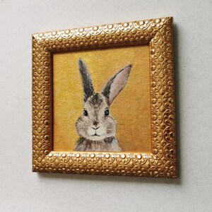 Close-up of hand-painted rabbit face on gold-textured canvas.