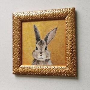 Bunny painting with vintage-style frame on neutral wall.