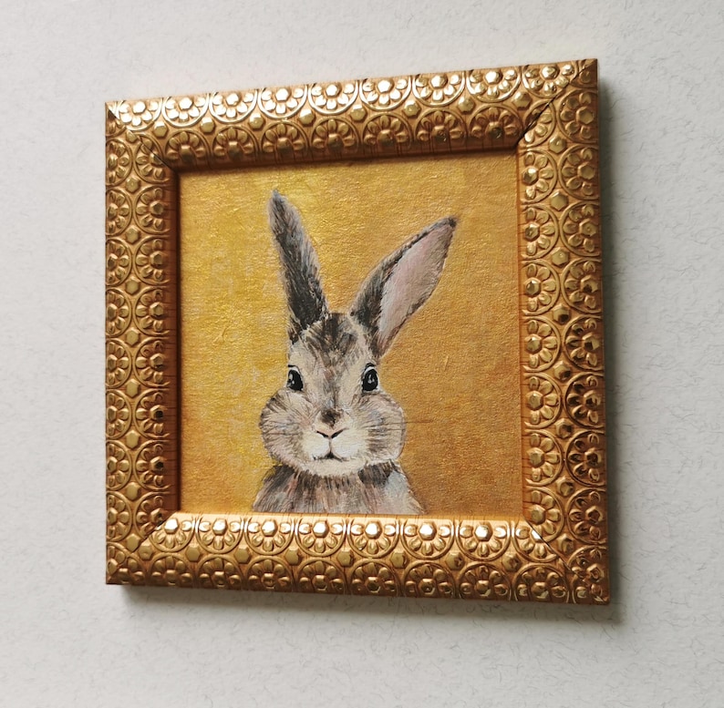 Bunny painting with vintage-style frame on neutral wall.
