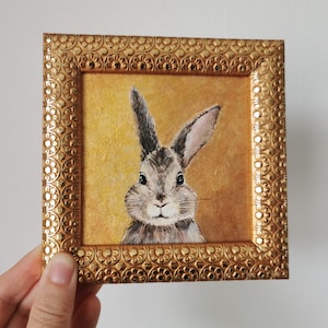 Side angle of framed bunny artwork in ornate plastic frame.