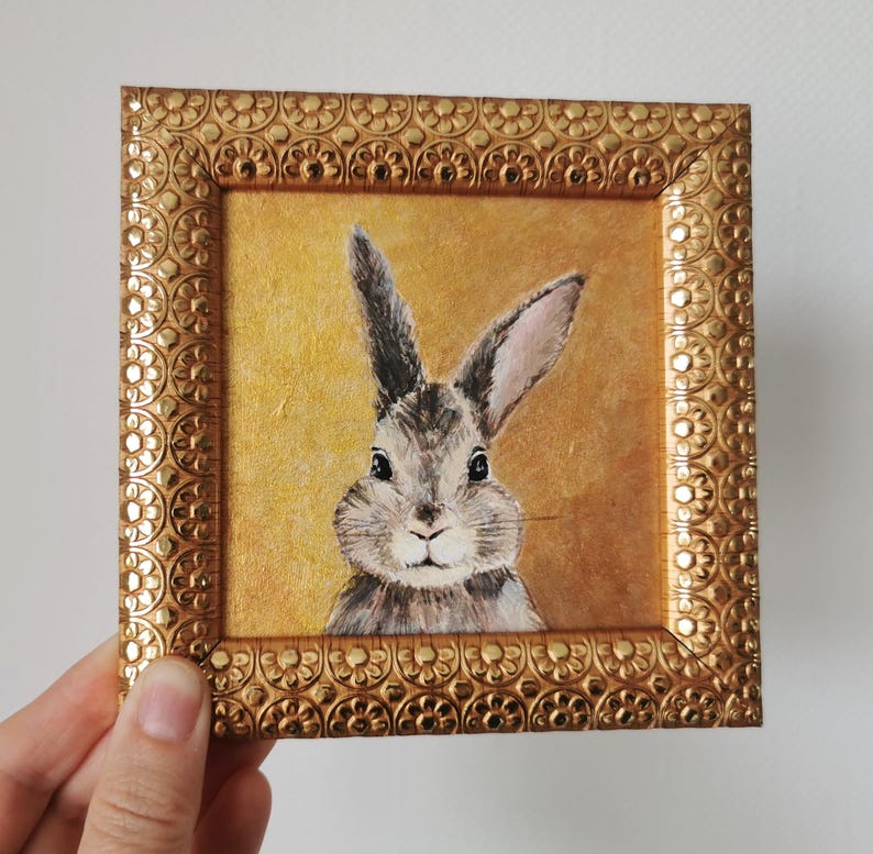 Side angle of framed bunny artwork in ornate plastic frame.