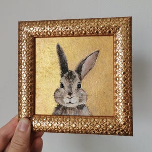 Bunny acrylic painting with vintage-style frame on neutral wall.