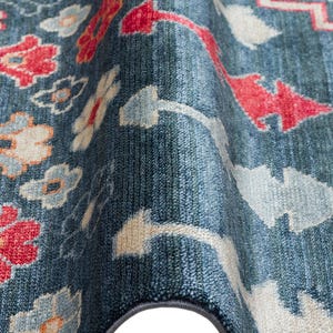 K&ouml;nnte beinhalten: Nahaufnahme eines blauen Teppichs mit Blumenmuster. Der Teppich hat rote, wei&szlig;e und hellblaue Blumen- und geometrische Designs. Der Teppich hat einen dunkelblauen Rand und eine strukturierte Oberfl&auml;che.