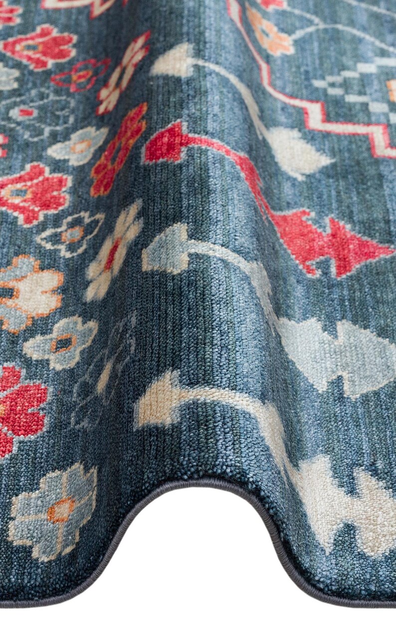 K&ouml;nnte beinhalten: Nahaufnahme eines blauen Teppichs mit Blumenmuster. Der Teppich hat rote, wei&szlig;e und hellblaue Blumen- und geometrische Designs. Der Teppich hat einen dunkelblauen Rand und eine strukturierte Oberfl&auml;che.