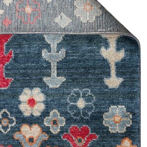 K&ouml;nnte beinhalten: Nahaufnahme eines blauen Teppichs mit floralem Muster. Der Teppich hat einen marineblauen Hintergrund mit roten, orangefarbenen und cremefarbenen Blumendesigns. Der Rand ist umgeschlagen und zeigt eine hellere blaue R&uuml;ckseite.