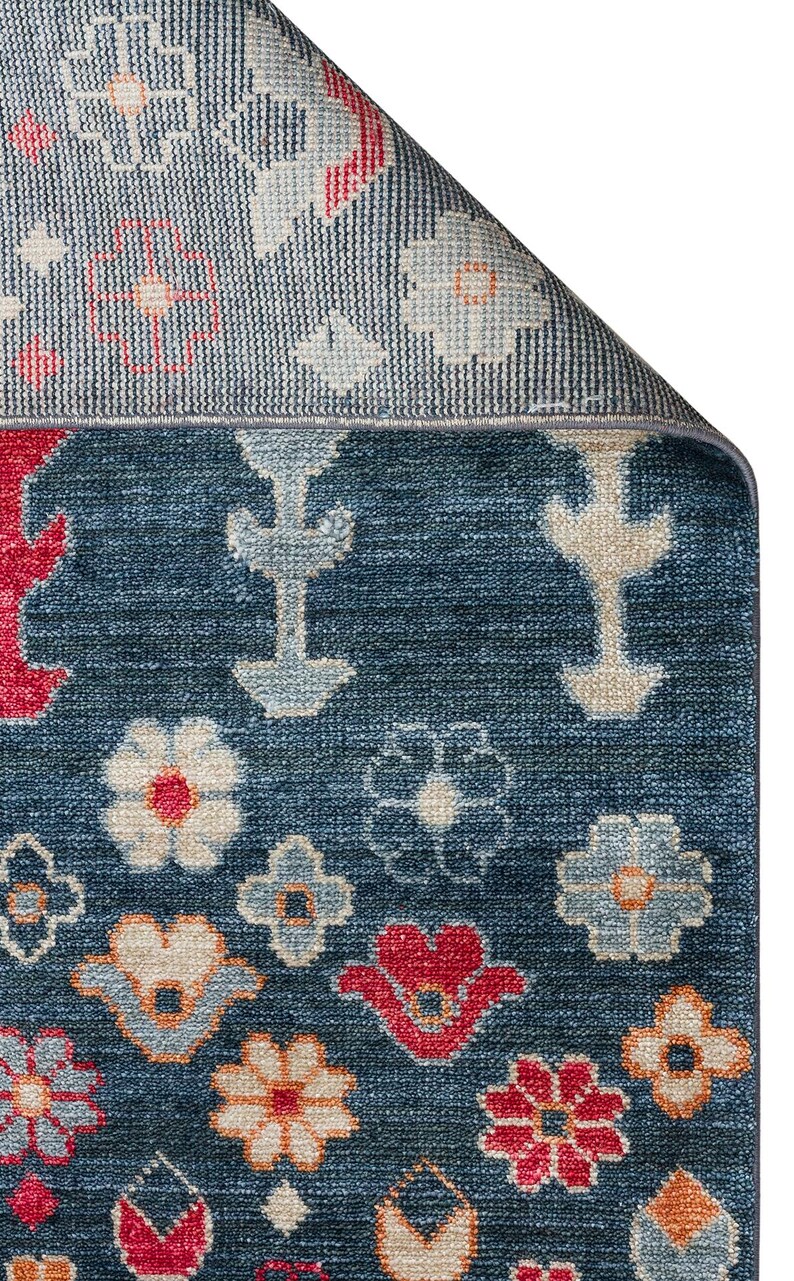 K&ouml;nnte beinhalten: Nahaufnahme eines blauen Teppichs mit floralem Muster. Der Teppich hat einen marineblauen Hintergrund mit roten, orangefarbenen und cremefarbenen Blumendesigns. Der Rand ist umgeschlagen und zeigt eine hellere blaue R&uuml;ckseite.