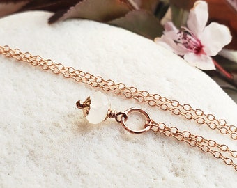 Puede incluir: Un delicado collar de cadena de oro rosa con un solo colgante de piedra blanca. El collar es de capas y presenta un pequeño amuleto circular.