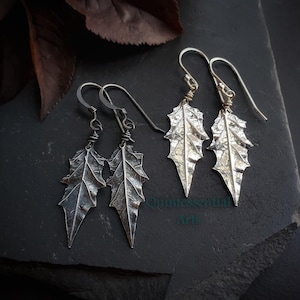 May include: A pair of silver leaf earrings with a textured finish. The earrings are hanging from silver hooks.