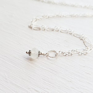 May include: A delicate silver chain necklace with a single white moonstone pendant.