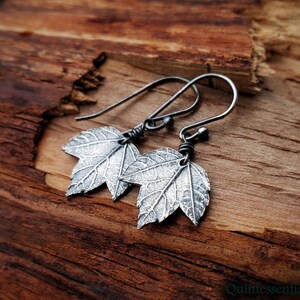 Puede incluir: Un par de pendientes de plata con un diseño de hoja texturizada. Los pendientes están hechos de plata de ley y tienen un aspecto delicado y femenino.