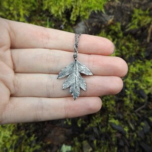 Puede incluir: Un collar con un colgante de hoja de plata en una cadena delicada. La hoja est&aacute; detallada con una superficie texturizada, lo que le da un aspecto realista.