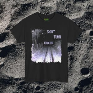 This analog horror-inspired T-shirt features the phrase “DON’T TURN AROUND” printed across a dark, eerie forest road under moonlight. On the other side, a creepy, distorted bunny character stares with a wide unsettling grin. The design blends glitchcore, VHS static, and nightmare-style textures for a perfect horror aesthetic. Printed on soft, high-quality fabric, ideal for horror fans and lovers of dark surreal art.