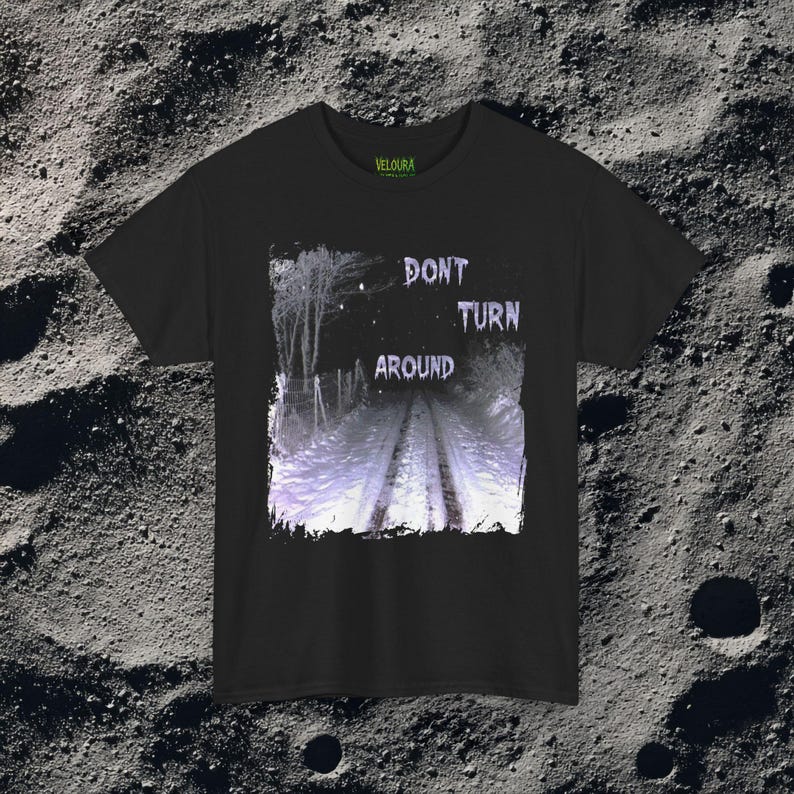 This analog horror-inspired T-shirt features the phrase “DON’T TURN AROUND” printed across a dark, eerie forest road under moonlight. On the other side, a creepy, distorted bunny character stares with a wide unsettling grin. The design blends glitchcore, VHS static, and nightmare-style textures for a perfect horror aesthetic. Printed on soft, high-quality fabric, ideal for horror fans and lovers of dark surreal art.