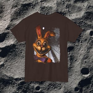 This analog horror-inspired T-shirt features the phrase “DON’T TURN AROUND” printed across a dark, eerie forest road under moonlight. On the other side, a creepy, distorted bunny character stares with a wide unsettling grin. The design blends glitchcore, VHS static, and nightmare-style textures for a perfect horror aesthetic. Printed on soft, high-quality fabric, ideal for horror fans and lovers of dark surreal art.