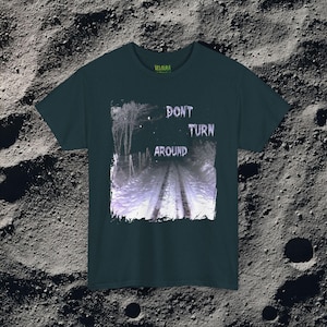 This analog horror-inspired T-shirt features the phrase “DON’T TURN AROUND” printed across a dark, eerie forest road under moonlight. On the other side, a creepy, distorted bunny character stares with a wide unsettling grin. The design blends glitchcore, VHS static, and nightmare-style textures for a perfect horror aesthetic. Printed on soft, high-quality fabric, ideal for horror fans and lovers of dark surreal art.