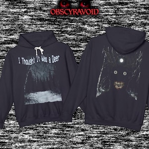 May include: A dark gray hooded sweatshirt featuring a graphic print of a forest scene with the text I Thought It Was a Deer on the front. The back displays a dark, shadowy figure with glowing eyes, sharp teeth, and a moonlit forest background.