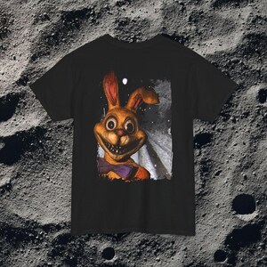 This analog horror-inspired T-shirt features the phrase “DON’T TURN AROUND” printed across a dark, eerie forest road under moonlight. On the other side, a creepy, distorted bunny character stares with a wide unsettling grin. The design blends glitchcore, VHS static, and nightmare-style textures for a perfect horror aesthetic. Printed on soft, high-quality fabric, ideal for horror fans and lovers of dark surreal art.