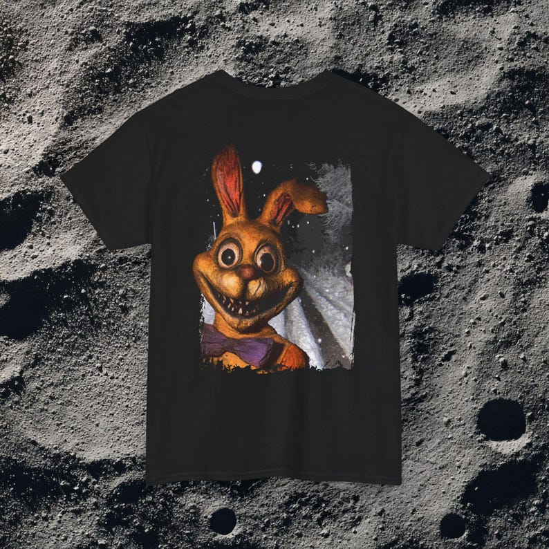 This analog horror-inspired T-shirt features the phrase “DON’T TURN AROUND” printed across a dark, eerie forest road under moonlight. On the other side, a creepy, distorted bunny character stares with a wide unsettling grin. The design blends glitchcore, VHS static, and nightmare-style textures for a perfect horror aesthetic. Printed on soft, high-quality fabric, ideal for horror fans and lovers of dark surreal art.