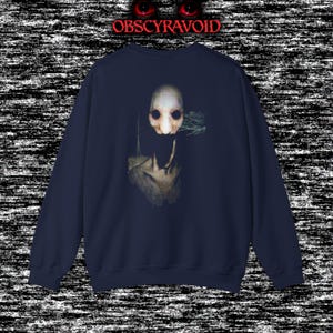 This analog horror sweatshirt features a chilling dual-sided design. The front shows a dark, grainy forest scene with glitchy text reading “I can feel it breathing behind me.” The back displays a disturbing pale creature emerging from the shadows, created with VHS static, noise, and eerie textures. Perfect for horror fans who love unsettling artwork, dark aesthetics, creepy forest themes, and lost-footage style designs.