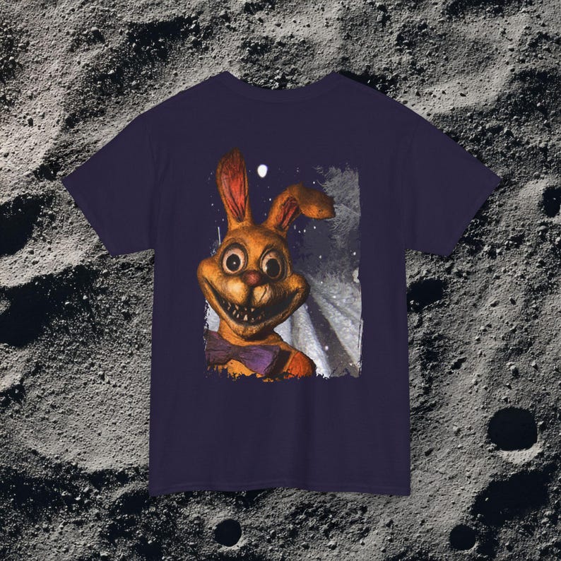 This analog horror-inspired T-shirt features the phrase “DON’T TURN AROUND” printed across a dark, eerie forest road under moonlight. On the other side, a creepy, distorted bunny character stares with a wide unsettling grin. The design blends glitchcore, VHS static, and nightmare-style textures for a perfect horror aesthetic. Printed on soft, high-quality fabric, ideal for horror fans and lovers of dark surreal art.