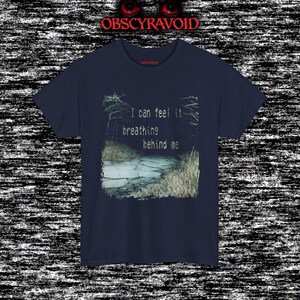 This analog horror T-shirt features a distressed VHS-style forest scene with eerie text overlay, combined with a terrifying pale mask-like creature emerging from darkness. Grainy textures, glitch effects, and cold blue tones create a creepy lost-footage atmosphere. Printed on a soft, high-quality shirt perfect for horror fans, dark aesthetic lovers, and anyone who enjoys unsettling, cinematic artwork.