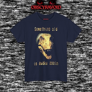 This analog horror–inspired T-shirt features a terrifying decayed dinosaur with human-like eyes and sharp teeth under the phrase “Something old is awake again.” The design combines VHS-style grain, eerie lighting, and vintage texture to create a haunting prehistoric horror vibe. Perfect for analog horror fans, dinosaur lovers, and retro-style collectors. Printed on high-quality fabric for lasting comfort and style.