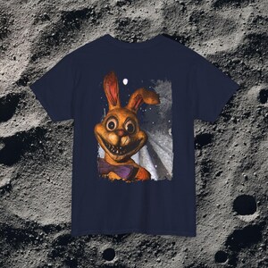 This analog horror-inspired T-shirt features the phrase “DON’T TURN AROUND” printed across a dark, eerie forest road under moonlight. On the other side, a creepy, distorted bunny character stares with a wide unsettling grin. The design blends glitchcore, VHS static, and nightmare-style textures for a perfect horror aesthetic. Printed on soft, high-quality fabric, ideal for horror fans and lovers of dark surreal art.