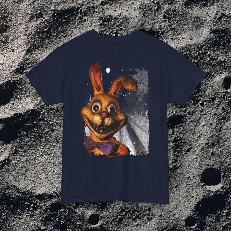 This analog horror-inspired T-shirt features the phrase “DON’T TURN AROUND” printed across a dark, eerie forest road under moonlight. On the other side, a creepy, distorted bunny character stares with a wide unsettling grin. The design blends glitchcore, VHS static, and nightmare-style textures for a perfect horror aesthetic. Printed on soft, high-quality fabric, ideal for horror fans and lovers of dark surreal art.