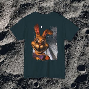 This analog horror-inspired T-shirt features the phrase “DON’T TURN AROUND” printed across a dark, eerie forest road under moonlight. On the other side, a creepy, distorted bunny character stares with a wide unsettling grin. The design blends glitchcore, VHS static, and nightmare-style textures for a perfect horror aesthetic. Printed on soft, high-quality fabric, ideal for horror fans and lovers of dark surreal art.