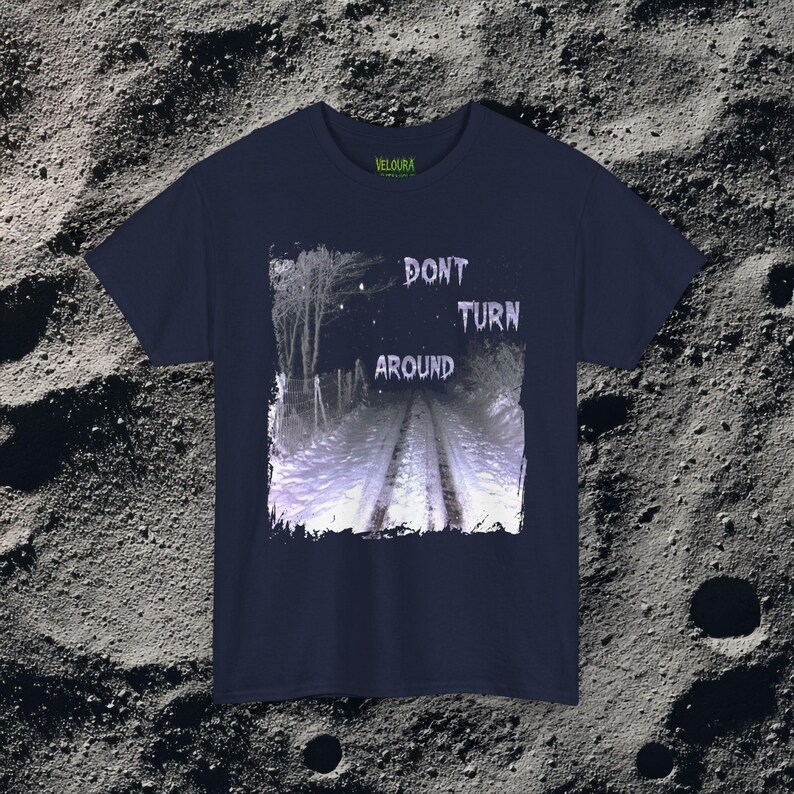 This analog horror-inspired T-shirt features the phrase “DON’T TURN AROUND” printed across a dark, eerie forest road under moonlight. On the other side, a creepy, distorted bunny character stares with a wide unsettling grin. The design blends glitchcore, VHS static, and nightmare-style textures for a perfect horror aesthetic. Printed on soft, high-quality fabric, ideal for horror fans and lovers of dark surreal art.
