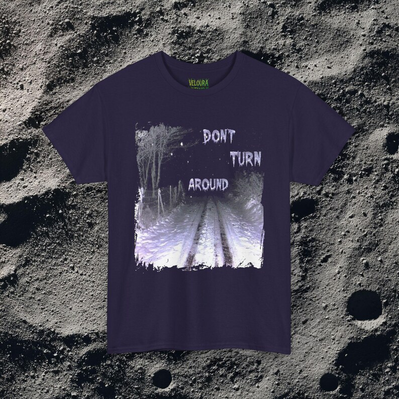 This analog horror-inspired T-shirt features the phrase “DON’T TURN AROUND” printed across a dark, eerie forest road under moonlight. On the other side, a creepy, distorted bunny character stares with a wide unsettling grin. The design blends glitchcore, VHS static, and nightmare-style textures for a perfect horror aesthetic. Printed on soft, high-quality fabric, ideal for horror fans and lovers of dark surreal art.
