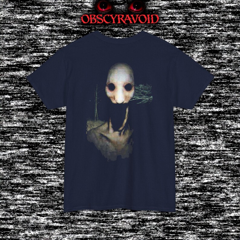 This analog horror T-shirt features a distressed VHS-style forest scene with eerie text overlay, combined with a terrifying pale mask-like creature emerging from darkness. Grainy textures, glitch effects, and cold blue tones create a creepy lost-footage atmosphere. Printed on a soft, high-quality shirt perfect for horror fans, dark aesthetic lovers, and anyone who enjoys unsettling, cinematic artwork.