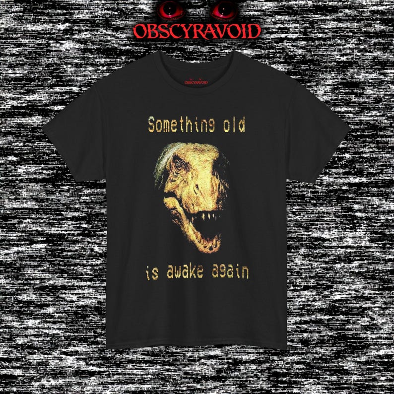 This analog horror–inspired T-shirt features a terrifying decayed dinosaur with human-like eyes and sharp teeth under the phrase “Something old is awake again.” The design combines VHS-style grain, eerie lighting, and vintage texture to create a haunting prehistoric horror vibe. Perfect for analog horror fans, dinosaur lovers, and retro-style collectors. Printed on high-quality fabric for lasting comfort and style.