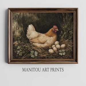 Può includere: Una stampa incorniciata raffigurante una gallina in un nido con uova. La gallina ha piume marrone chiaro e bianche, una cresta rossa ed è circondata da fieno e vegetazione. La stampa è in una cornice di legno scuro. Il testo in basso recita "MANITOU ART PRINTS."